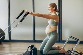 donna incinta che esige un esercizio di pilates con il Reformer per il rinforzo delle braccia