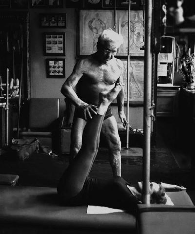 Joseph Pilates alle prese con una sua allieva in u n esercizio di allungamento della catena posteriore
